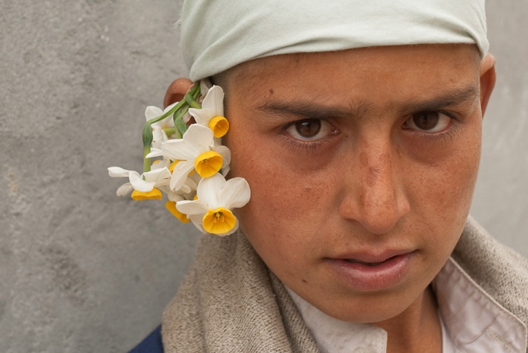 Garoto usa um punhado de flores selvagens atrás da orelha, na província de Kunar, durante cerimônia fúnebre. (Foto: James Lee)